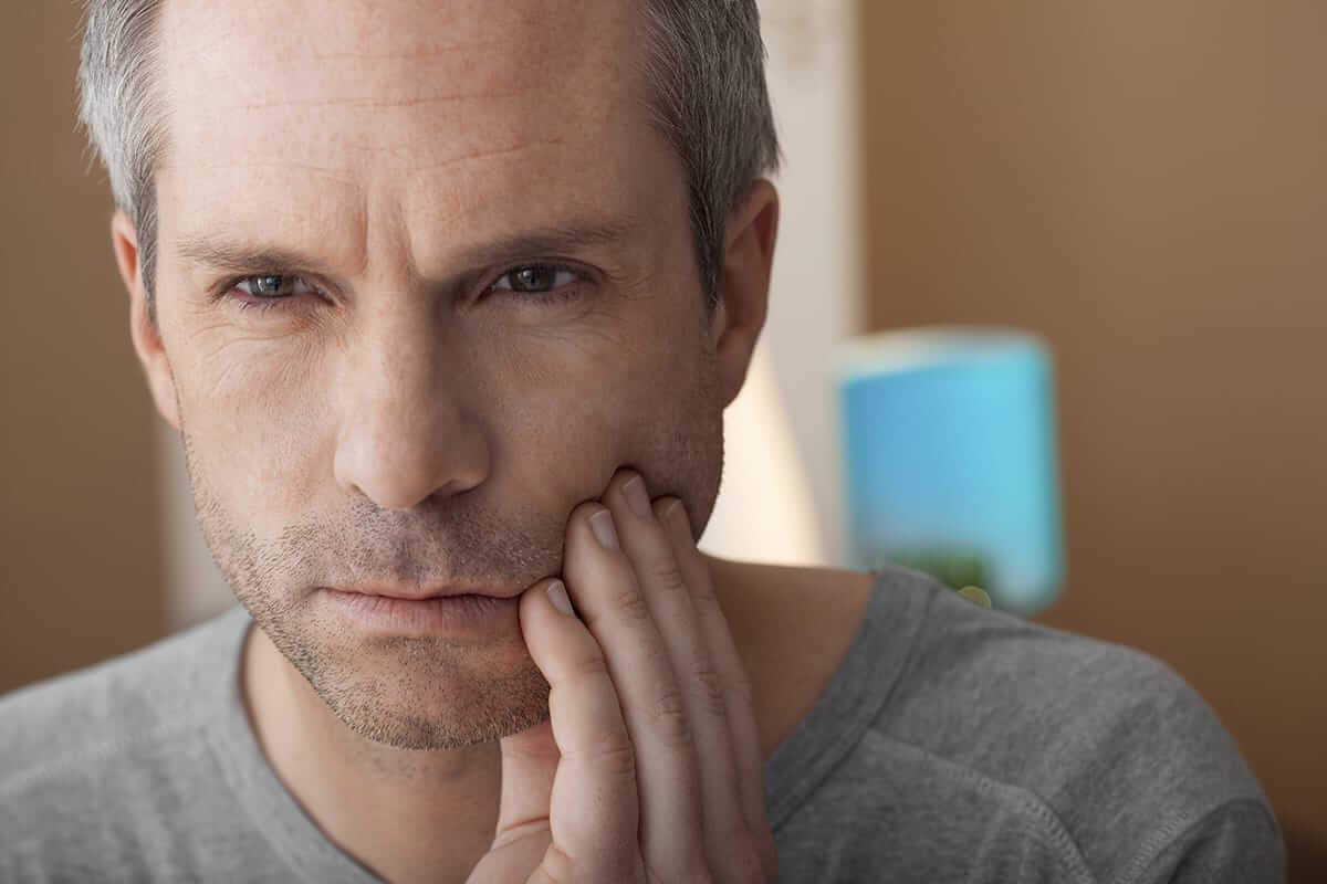 middle aged man holds side of his mouth because of tooth impaction pain
